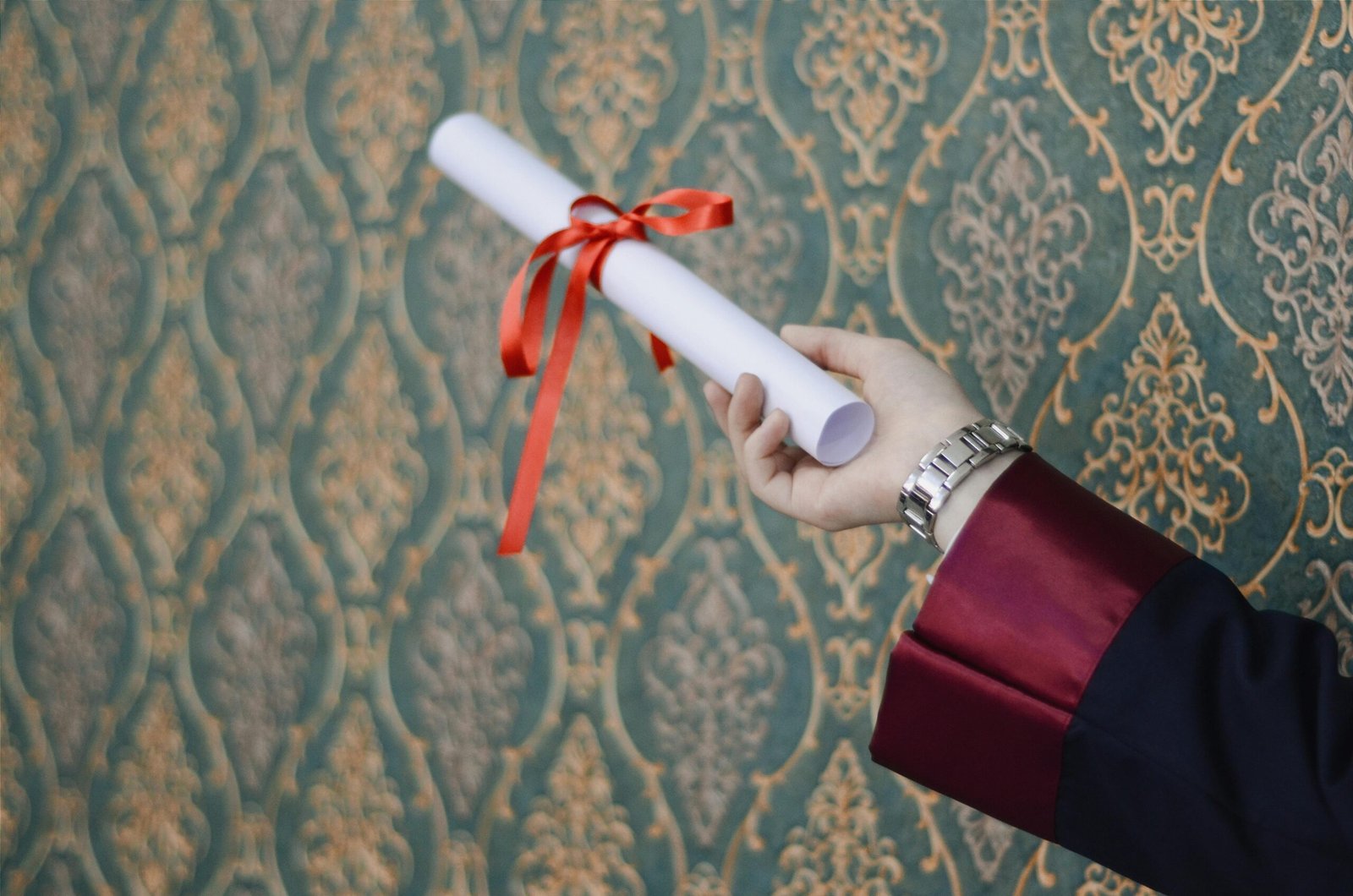 A graduate's hand holding a diploma with red ribbon, symbolizing achievement.